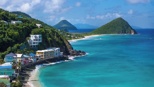 A coastal resort with multiple buildings, a beach, and a mountainous backdrop. - VILLA SANTORINI - walk to beach and restaurants from this luxurious masterpiece (Tortola)