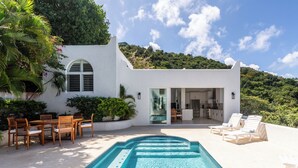 A modern house with a swimming pool, outdoor seating, and a kitchen visible through glass doors. - VILLA SANTORINI - walk to beach and restaurants from this luxurious masterpiece (Tortola)