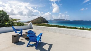A terrace with two blue Adirondack chairs and a concrete table, overlooking a beach and ocean with a mountainous backdrop. - VILLA SANTORINI - walk to beach and restaurants from this luxurious masterpiece (Tortola)