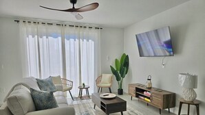 A living room with a sofa, chairs, a coffee table, a TV, and a plant.