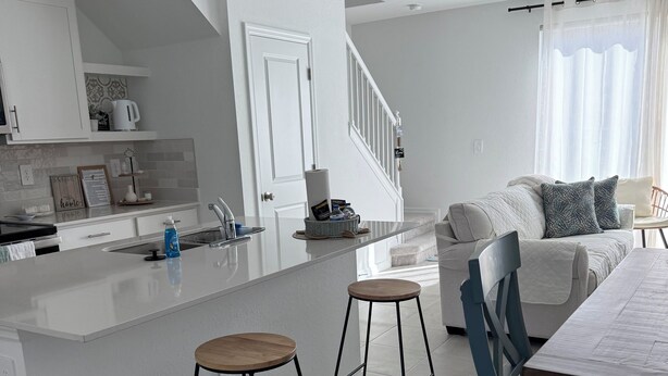 A modern kitchen with white cabinetry, a central island with stools, and a dining area with a table and chairs.
