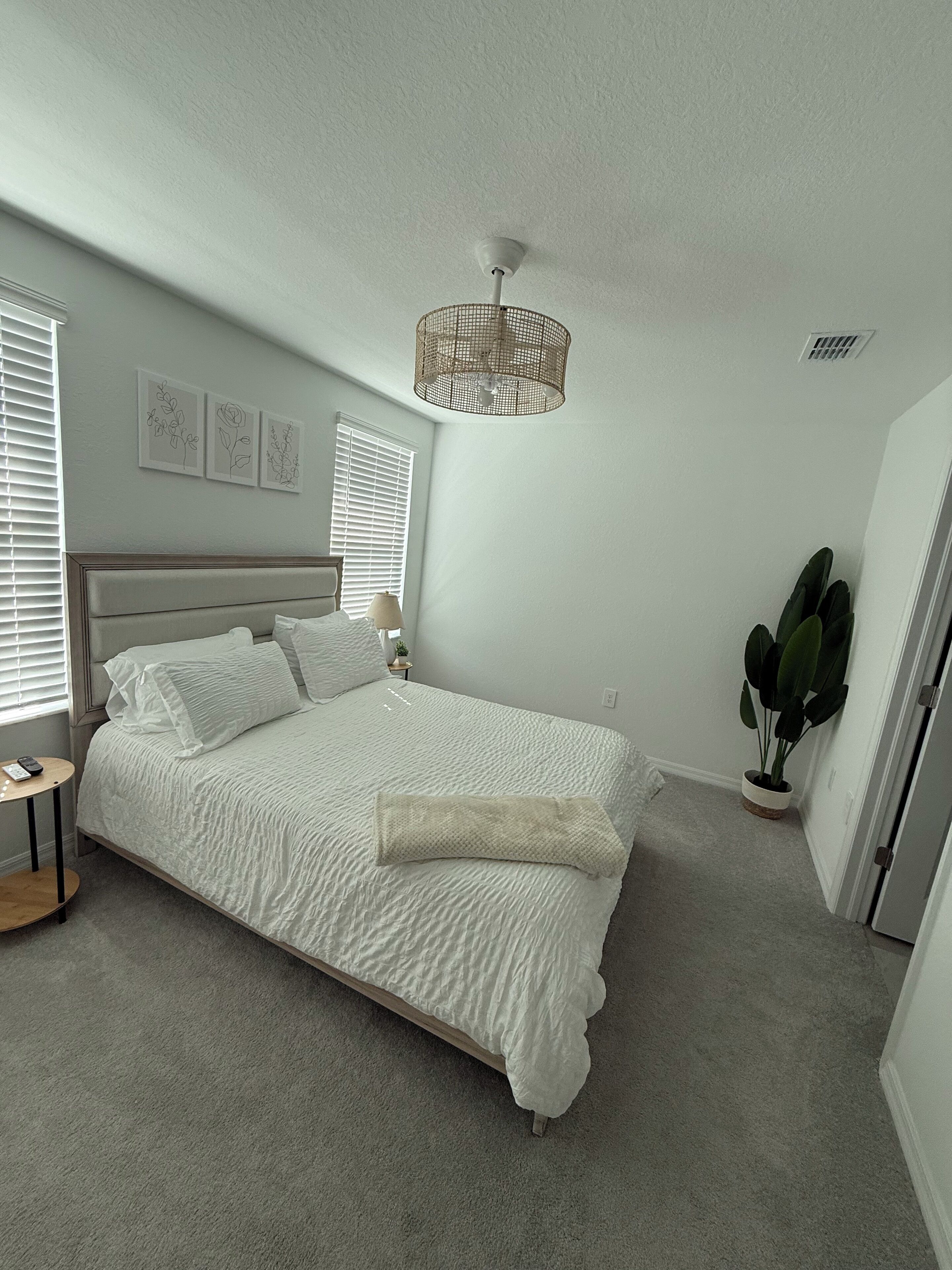 A bedroom with a large bed, a bedside table, a lamp, and a potted plant.