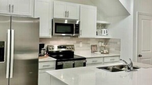 A modern kitchen with white cabinetry, stainless steel appliances, and a central island with a sink.