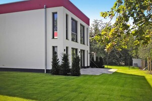 A modern building with a red roof and white walls, surrounded by a well-maintained lawn and trees.