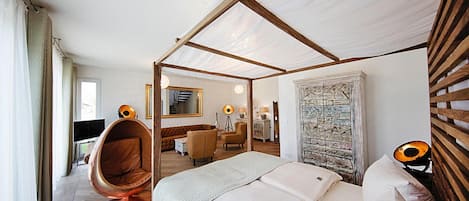 Habitación de hotel moderna con cama a dosel, una silla colgante, un escritorio y vistas de la ciudad.