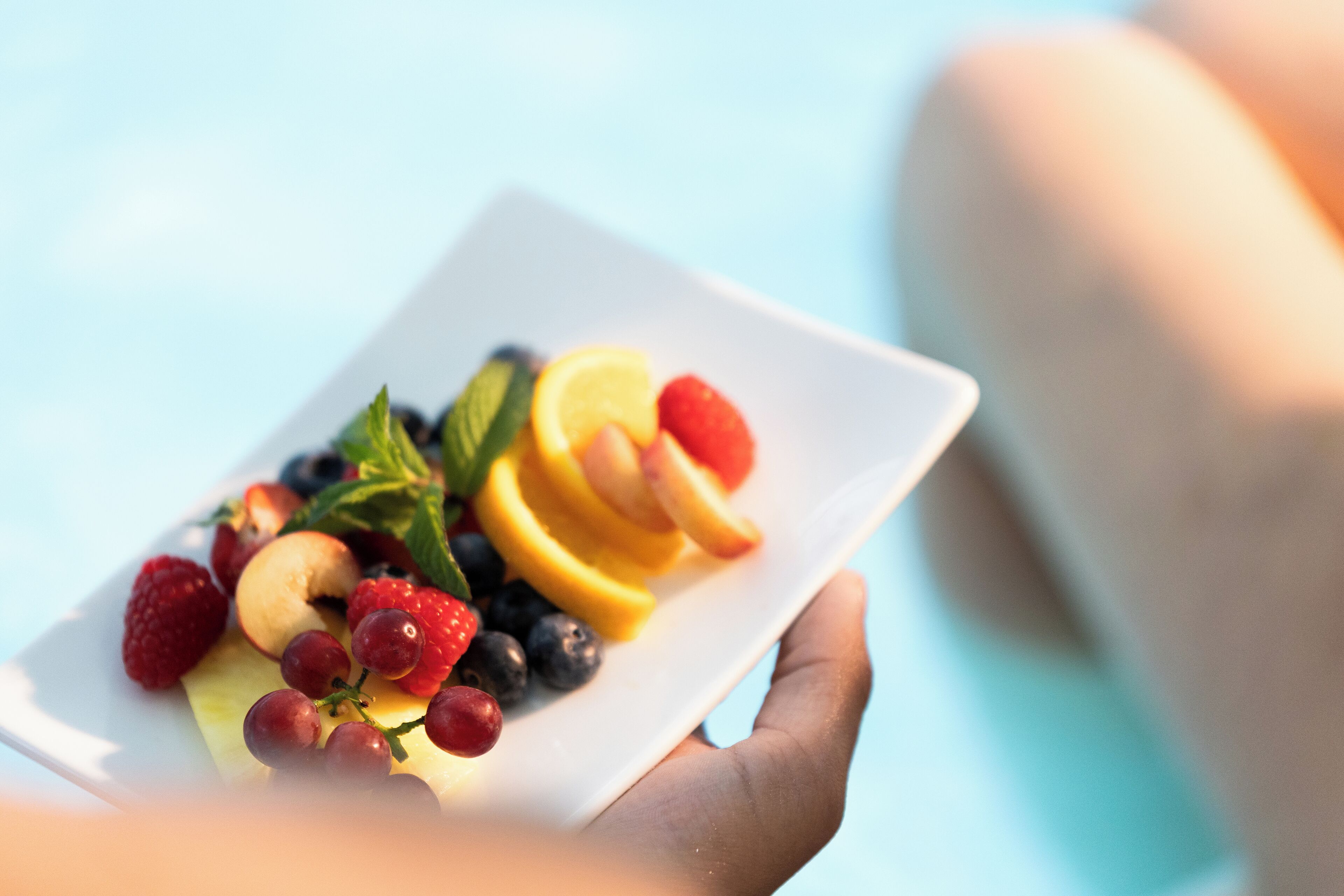 Een hand die een wit bord vasthoudt met gesneden fruit en bessen.