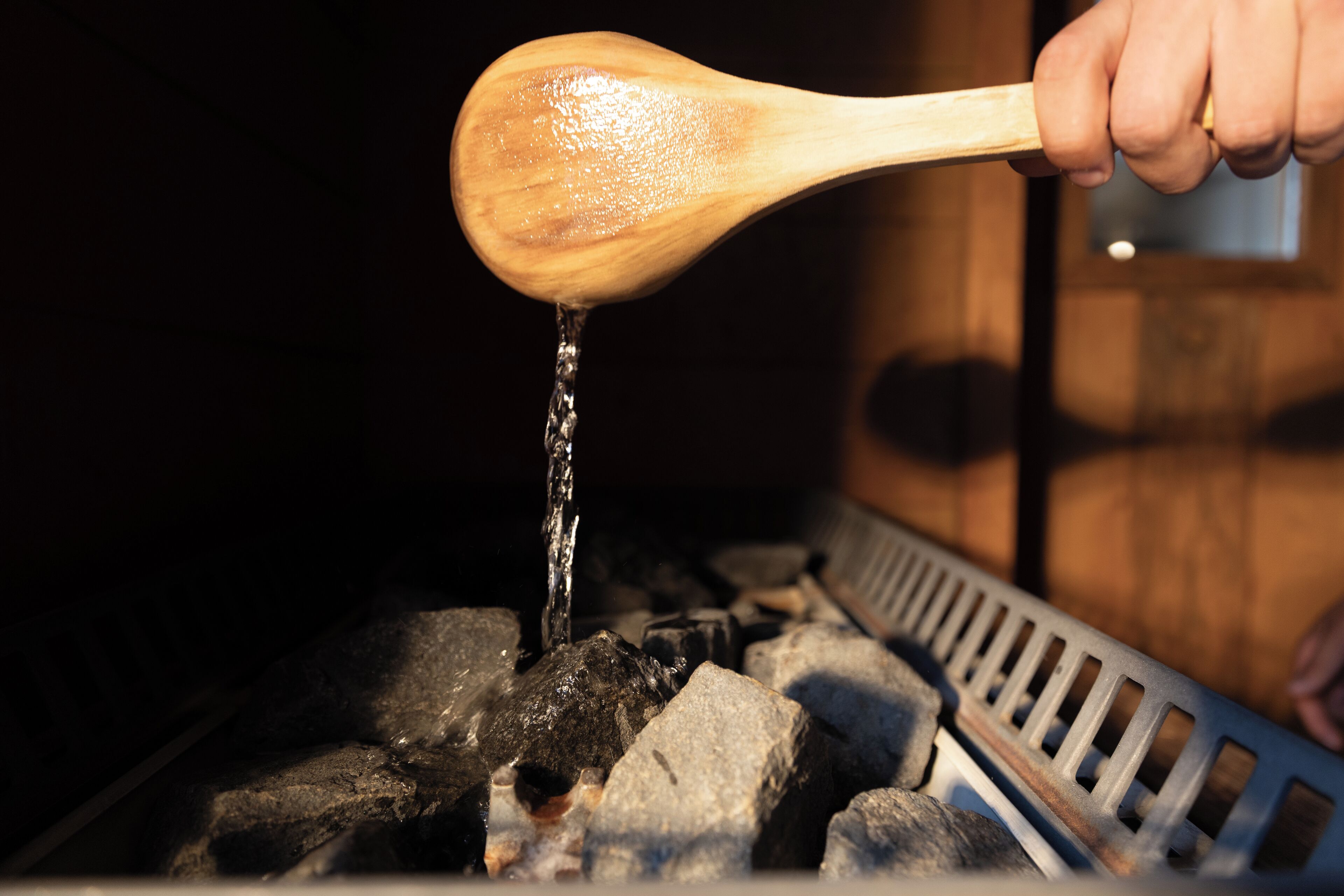 A wooden spoon pouring water onto charcoal in a grill.