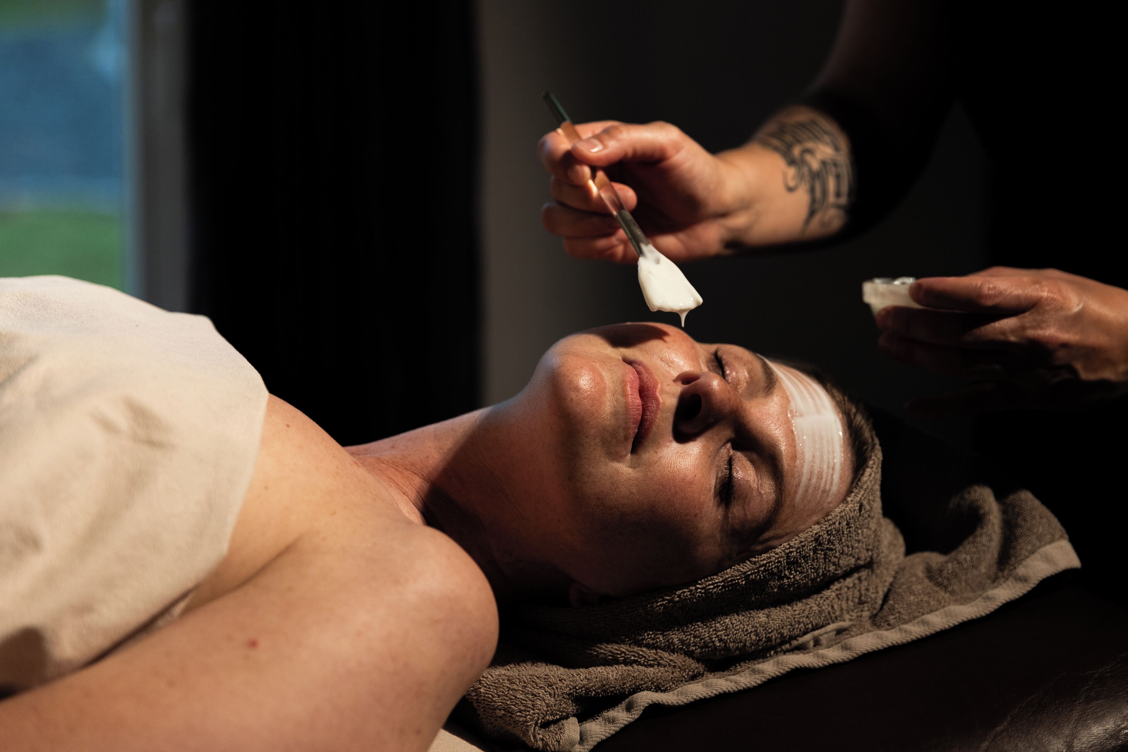 A person lying down with a towel around their neck, receiving a treatment from another person.