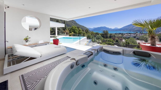Un área moderna de hidromasaje al aire libre con piscina, mobiliario blanco y una vista panorámica a las montañas.