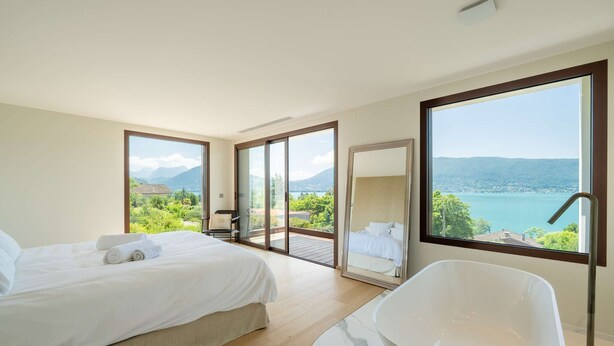 A modern hotel room with a large bed, a bathtub, and a balcony with a scenic view.