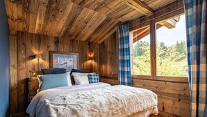 Een gezellige slaapkamer met een houten plafond, een groot bed met veel kussens, een nachtkastje met een lamp en een raam met gordijnen.