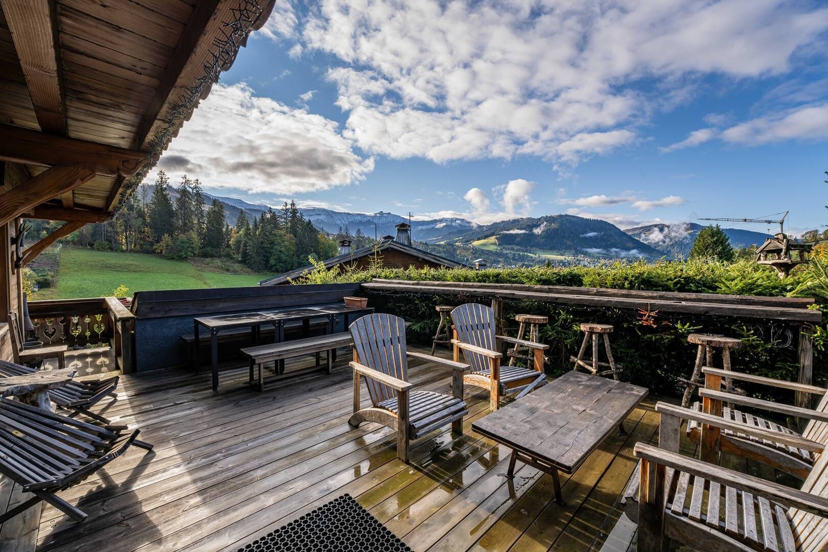 Une terrasse en bois avec des sièges d’extérieur, comprenant des chaises et des tables, offrant une vue sur un paysage montagneux.