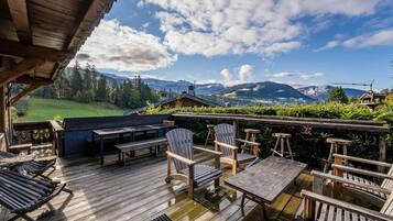 Une terrasse en bois avec des sièges d’extérieur, comprenant des chaises et des tables, offrant une vue sur un paysage montagneux.