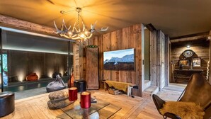 Een gezellige woonkamer met houten inrichting, een open haard, een televisie en een groot raam met uitzicht op een besneeerd landschap.