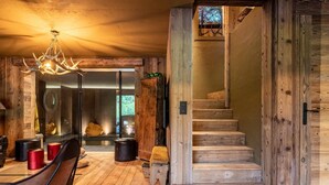 Een rustiek interieur met een houten trap, een eetruimte met een kroonluchter, en een uitzicht door een glazen deur.