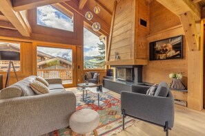 A spacious living area with a fireplace, comfortable seating, and large windows offering a view of the surrounding landscape. - Chalet du Jaillet (Demi-Quartier)