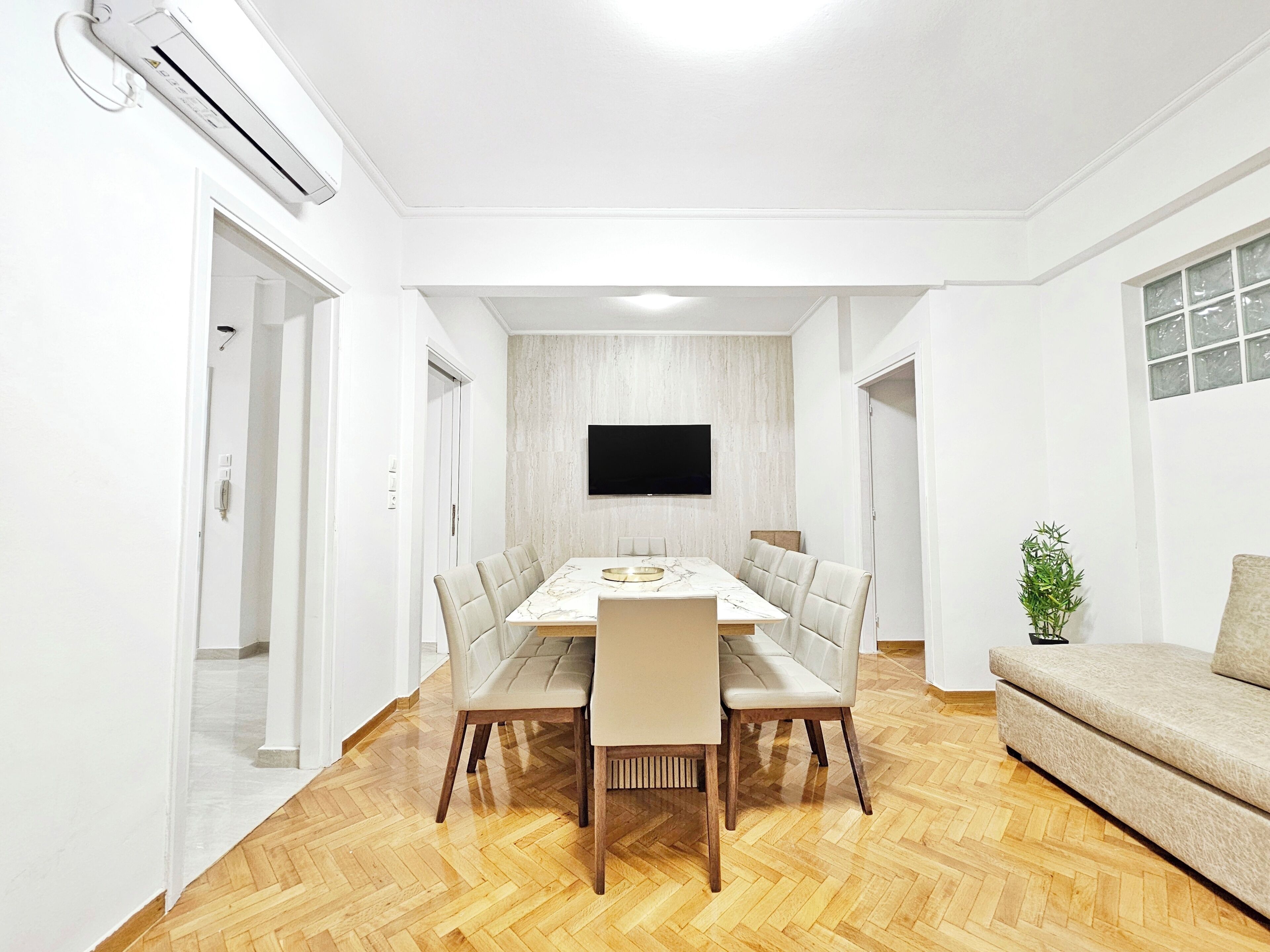 A modern dining room with a marble table, leather chairs, and a flat-screen TV mounted on the wall.