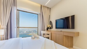 Une chambre d’hôtel avec un grand lit, un téléviseur fixé au mur, un bureau avec un miroir et une vue sur le paysage urbain par une grande fenêtre.