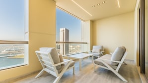 Un balcon moderne avec deux chaises blanches et une petite table, offrant une vue sur le paysage urbain et l’étendue d’eau.
