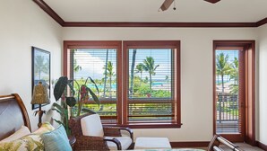 Une chambre à coucher comprenant un lit, une chaise, une table et de grandes fenêtres donnant sur des palmiers et une plage.