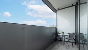Een balkon met een metalen hekwerk, een kleine ronde tafel met twee stoelen en een bloempot.