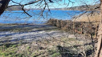 A lakeside view with a sandy beach, a wooden fence, and leafless trees.