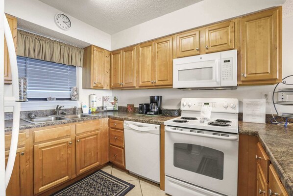 A kitchen with wooden cabinets, a microwave, a stove, a dishwasher, and a window with blinds.