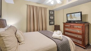 A hotel room with a bed, a television, a ceiling fan, and a wooden dresser. - Seaside Beach 5417 | Beachfront Condo w/ Pool, Sauna & Balcony Gulf (Orange Beach)