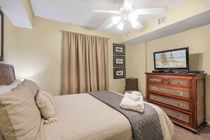 A hotel room with a bed, a television, a ceiling fan, and a wooden dresser. - Seaside Beach 5417 | Beachfront Condo w/ Pool, Sauna & Balcony Gulf (Orange Beach)