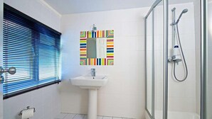 Un bagno con lavandino, uno specchio con cornice colorata, una doccia e una finestra con persiane.