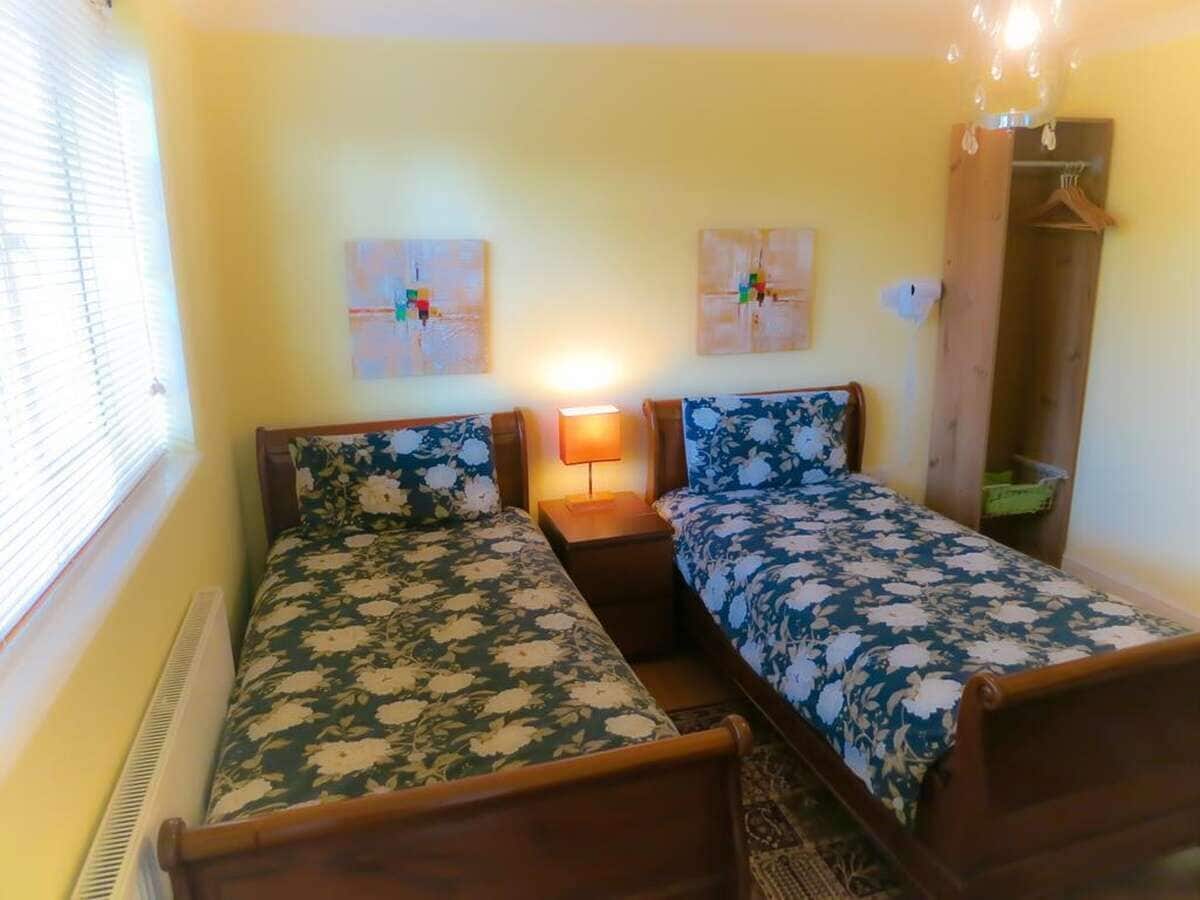 Une chambre avec deux lits simples, une table de chevet avec une lampe, un radiateur et une armoire en bois.