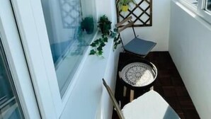 En liten balkong med ett trägolv, en vit stol, ett litet bord och en dekorativ avskärmning med växter.