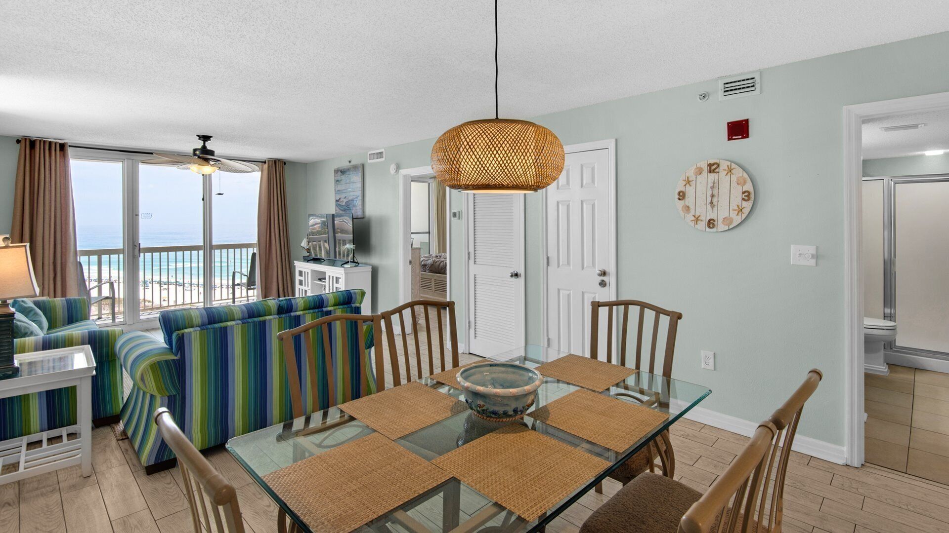 A living room with a glass dining table, striped sofa, and a view of the ocean.