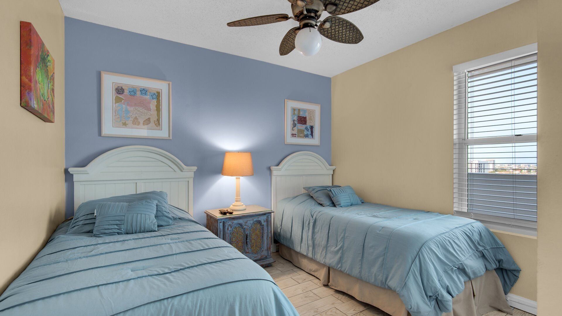 A bedroom with two beds, a ceiling fan, and a window with blinds.