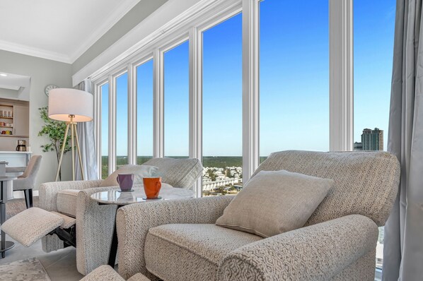 A modern living room with a sofa set, a coffee table, and a view of a cityscape through large windows.
