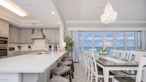 Una cocina moderna con una isla grande, muebles blancos y un comedor con vista al océano.