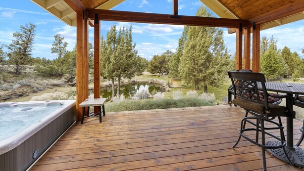 Una terraza de madera con un jacuzzi, una mesa y sillas, con vistas a un estanque y árboles.