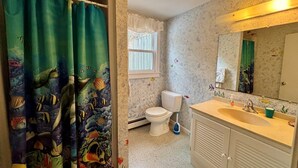 Un baño con inodoro, lavamanos y cortina de ducha con motivos marinos.