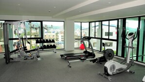 A gym with various exercise equipment, large windows, and a view of buildings. - Luxurious 45sqm Apartment in Peaceful Patong Location (Patong)