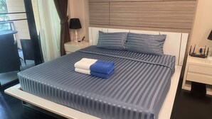 A modern hotel room with a large bed, a bedside table, a lamp, and a view of the outdoors. - Luxurious 45sqm Apartment in Peaceful Patong Location (Patong)