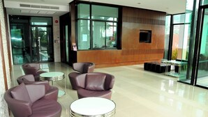 A modern lobby with leather sofas, a reception desk, and a glass wall offering a view of the outdoors. - Luxurious 45sqm Apartment in Peaceful Patong Location (Patong)