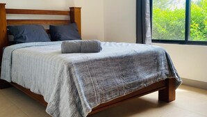 A neatly made bed with a grey blanket and pillows, a wooden headboard, and a window with curtains. - Charming 3-bedroom villa in fabulous Puerto Carrillo with WiFi, AC (Puerto Carrillo)