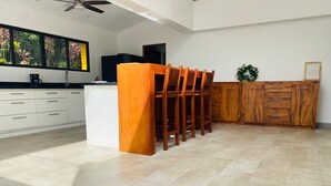 A modern kitchen with white cabinets, a wooden dining table, and a large window with a view of greenery. - Charming 3-bedroom villa in fabulous Puerto Carrillo with WiFi, AC (Puerto Carrillo)