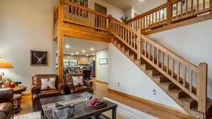 A spacious living room with a wooden staircase, leather furniture, and a kitchen in the background. - Comfort and Luxury at its best, Hot Tub 1 Dog. New Property (Blairsville)