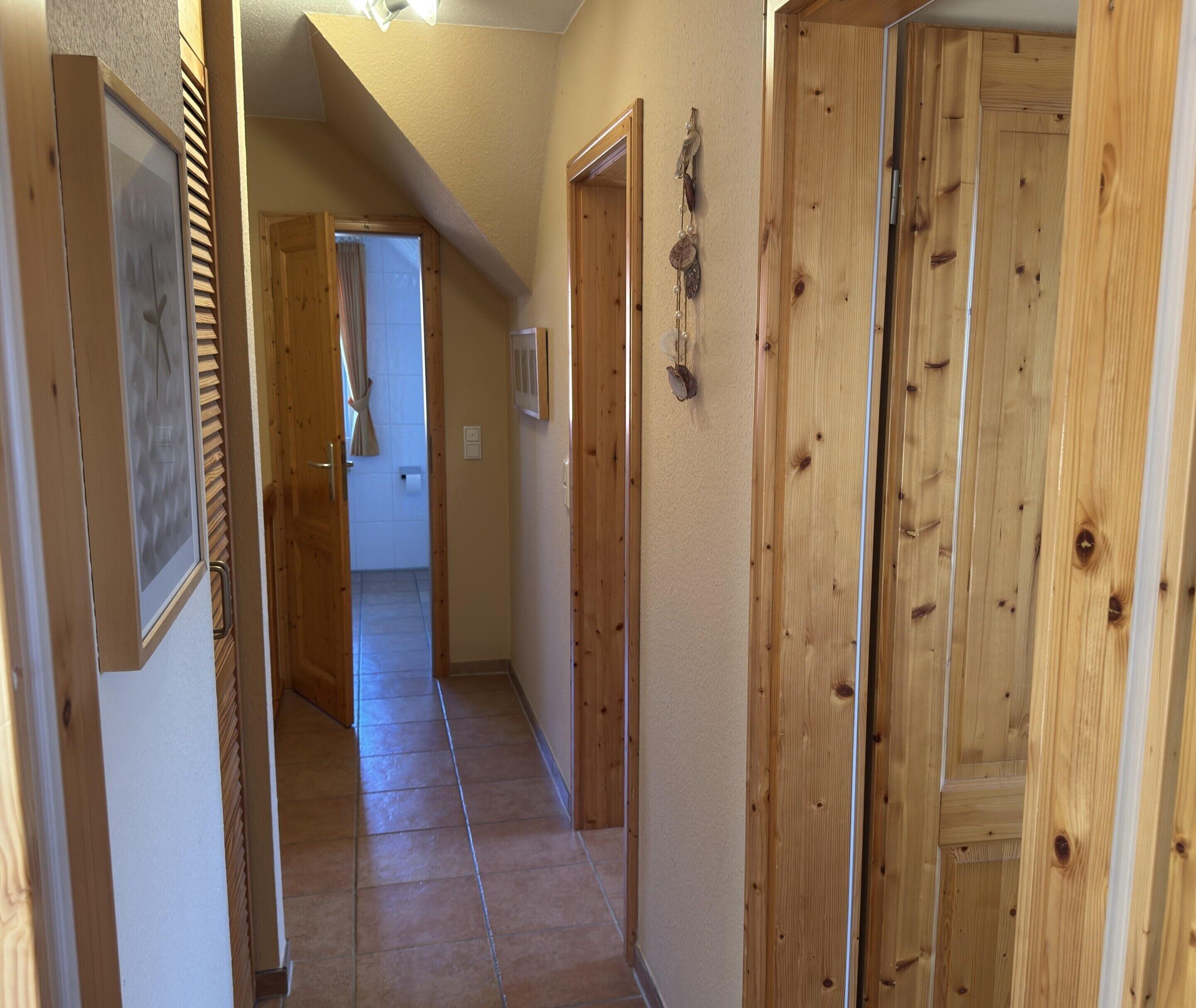 A narrow hallway with wooden doors and a tiled floor.