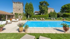 A swimming pool with lounge chairs, a stone tower, and a well-maintained garden.