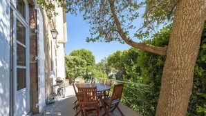 A patio with a round table and chairs, a grill, and a view of a garden with trees.