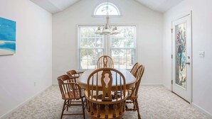 A dining room with a round wooden table and six chairs, large windows, and a door with a decorative glass panel. - 5 Min Walk to Nags Head Beach, Centrally Located! (Nags Head)