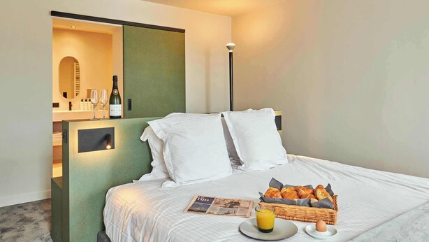 A hotel room with a bed, a breakfast tray with croissants, a newspaper, and a bottle of wine on the nightstand. - Luxurious townhouse in AAA location with nearby parking. (Brugge)