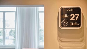 A wall-mounted clock displaying the date JUL 27, 2021, in a room with a window and a pink chair. - Luxurious townhouse in AAA location with nearby parking. (Brugge)